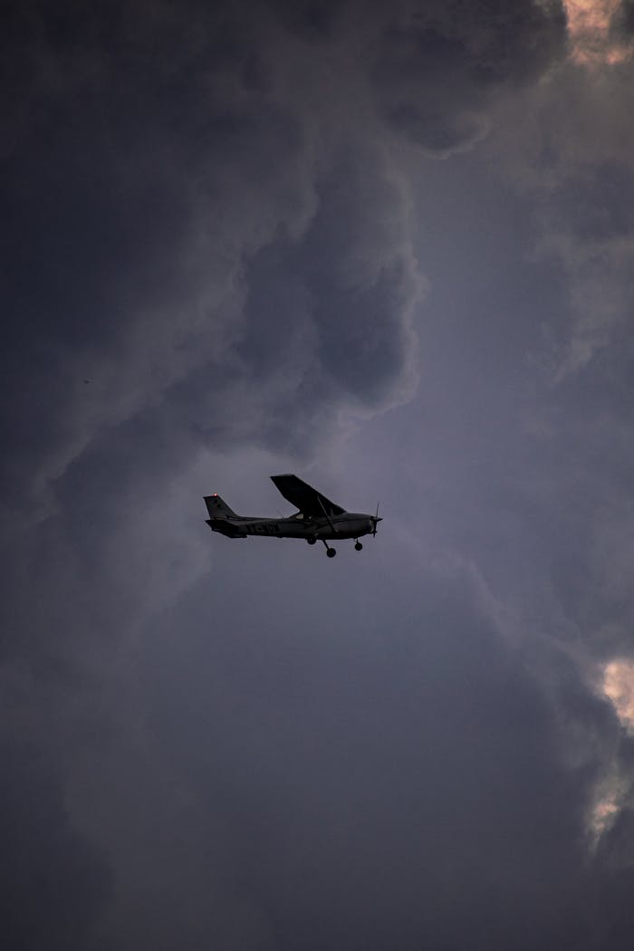 Silhouette of a small aircraft flying against a dramatic cloudy sky, showcasing aviation freedom.