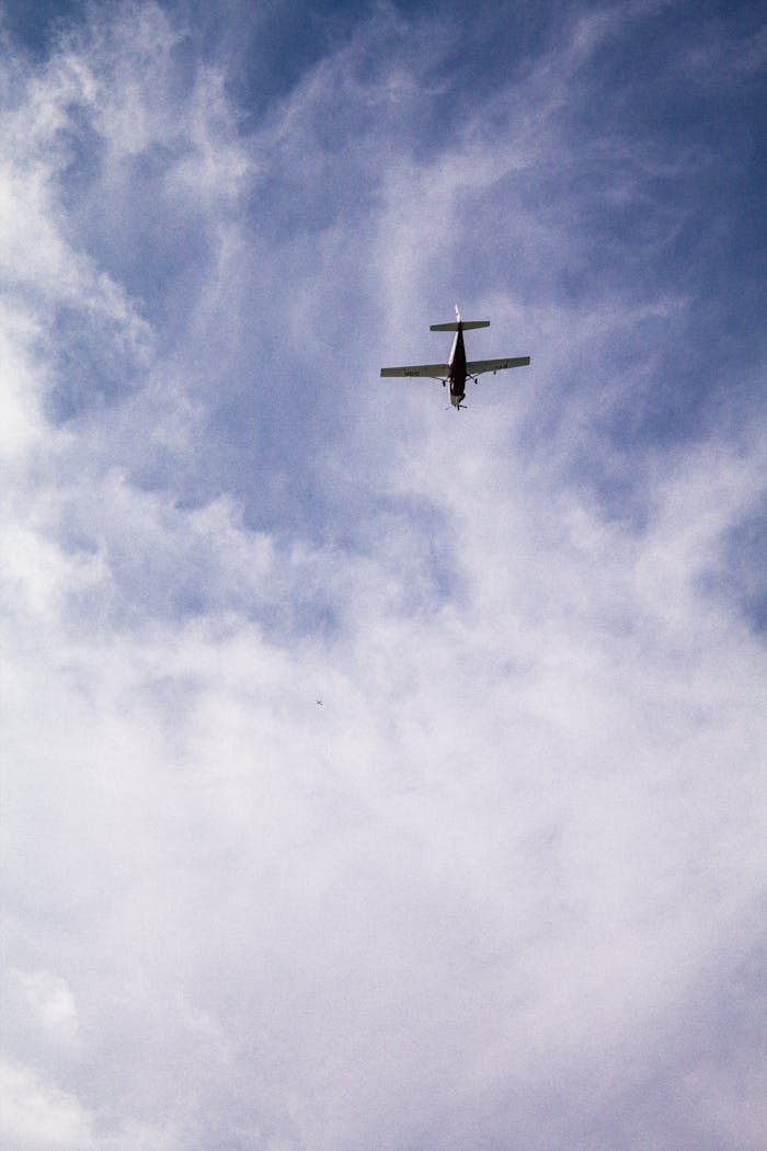 A small single-engine propeller plane flying high in a cloudy blue sky.